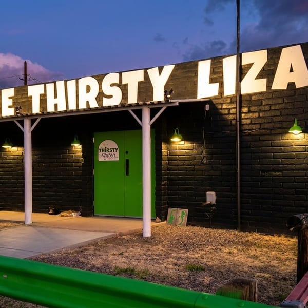 The Thirsty Lizard restaurant exterior at dusk, with a bright green door and illuminated sign.