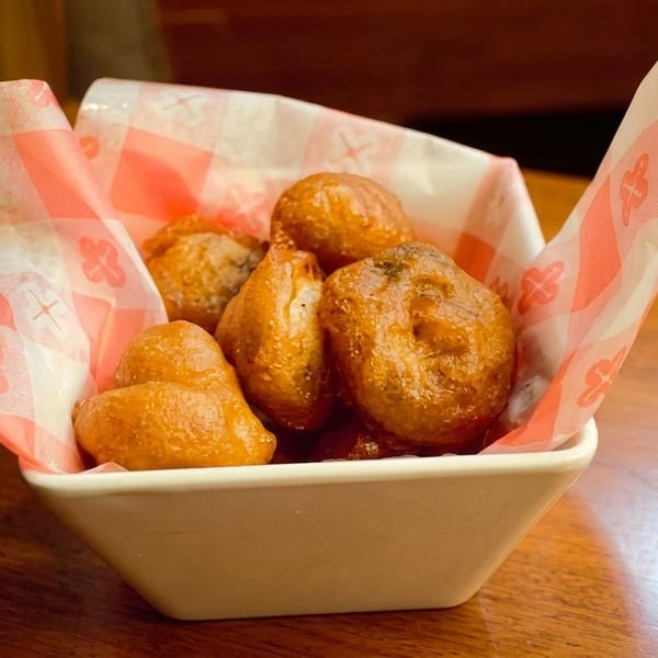 A white bowl filled with golden-brown hush puppies, lined with red and white checkered paper.