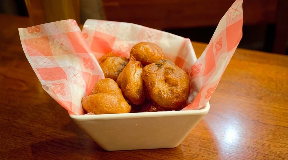 A white bowl filled with golden-brown hush puppies, lined with red and white checkered paper.