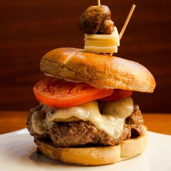 Gourmet burger with melted cheese, tomatoes, and a skewer of mushrooms and cheese on top.