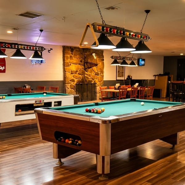 A spacious game room with two pool tables, a stone fireplace, and various seating areas.