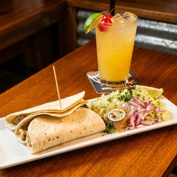 Two tacos with a side salad and a cocktail on a wooden table.