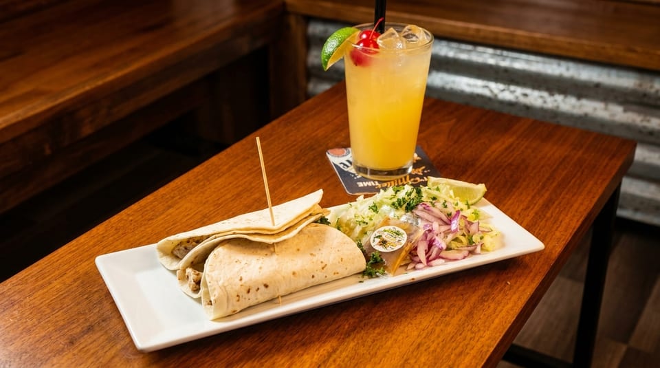 Two tacos with a side salad and a cocktail on a wooden table.